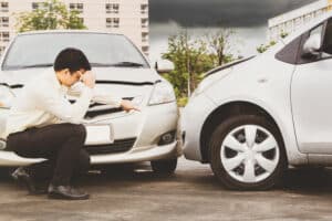 A businessman in a suit points toward a company car involved in a wreck in front of him.